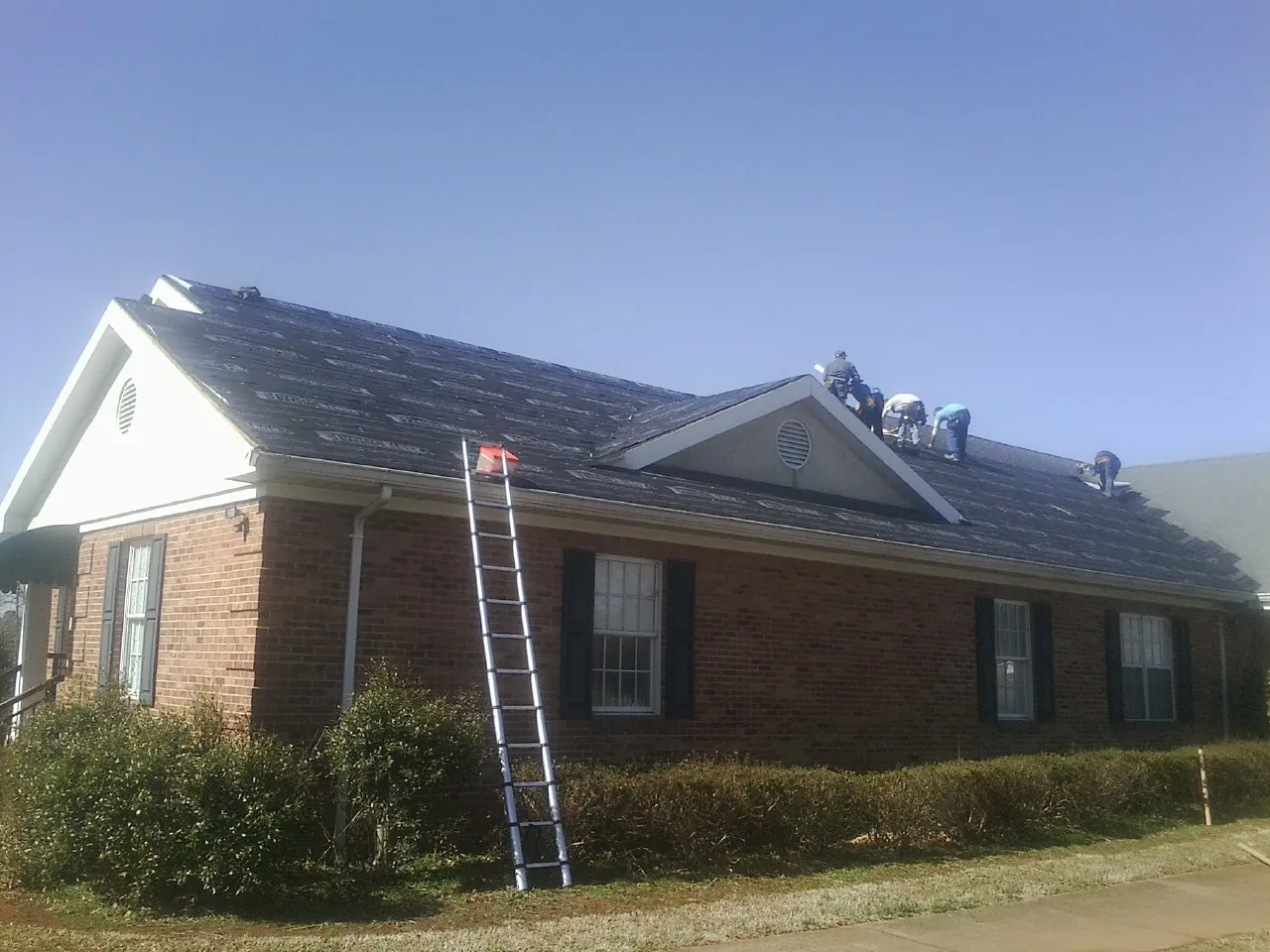 Crew tearing shingles off a brick ranch roof with a ladder set — Emergency Roof Repair work by our crew in Sugar Grove